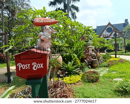 Charming garden scene featuring a decorative red post box with a cute rabbit statue holding a “Welcome