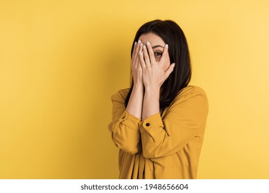 Charming Girl Covers Her Face With Her Hands, Only Her Eye Is Visible. Isolated On Orange Background, Place For Text.