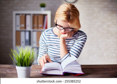 Charming girl sitting by wooden table and reading book