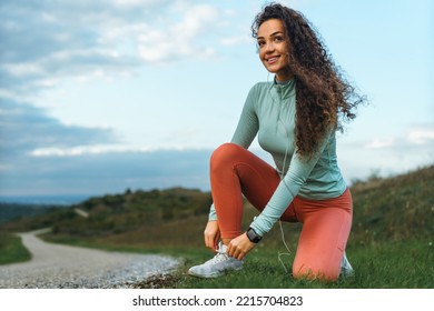 A charming girl stopped running to tie her shoelaces on the green grass while listening to music. - Powered by Shutterstock