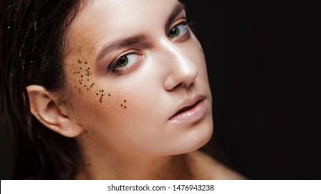Charming girl with trendy glitter makeup, fashionable make-up with gold glitter on the cheekbones and near the eyes.