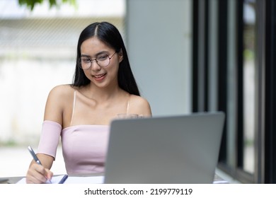 Charming And Good-humored Asian Woman Is Working On A Laptop In The Backyard. Working From Home.