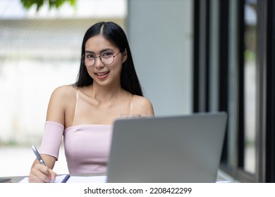 Charming And Good-humored Asian Woman Is Working On A Laptop In The Backyard. Working From Home.