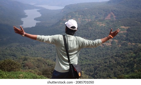 Charming Handsome. Confident Young Indian Man Enjoying And Travelling Solo In The Mountains With Selective Focus. Indian Guy Near A Waterfall Tourist Spot With Sunglasses. Travel Concept. 
