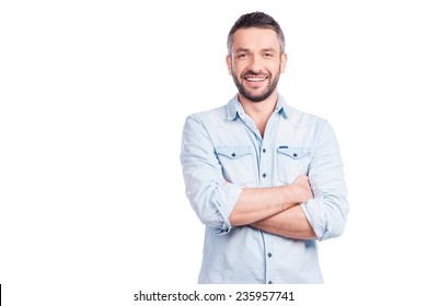 Charming handsome. Handsome young man in casual wear keeping arms crossed and smiling while standing isolated on white background