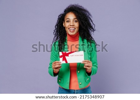 Charming happy charismatic excited young black curly woman 20s wears green shirt hold gift certificate coupon voucher card for store isolated on plain pastel light violet background studio portrait