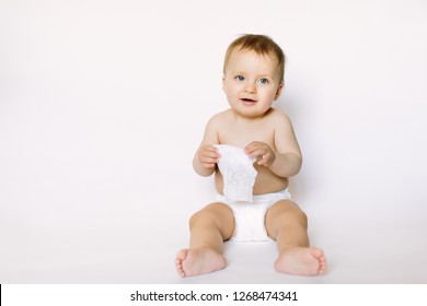 Charming happy little baby girl in white diaper holding wet wipe in her hands and sitting isolated on white background. Cleaning wipe, pure, clean