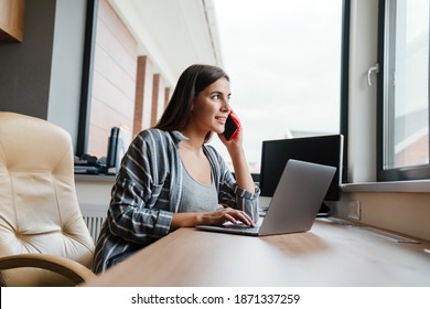 Charming happy woman talking on cellphone while working with laptop at home - Shutterstock ID 1871337259