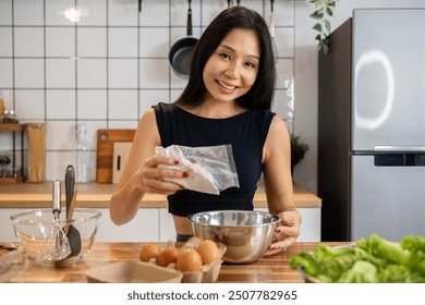 A charming, healthy Asian woman is making pancakes in the kitchen, adding pancake power mix to a bowl, cooking in the kitchen, smiling at the camera. people and domestic life concepts - Powered by Shutterstock