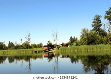 Charming houses lined along a riverbank with lush greenery under clear blue sky and gentle ripples on water - Powered by Shutterstock