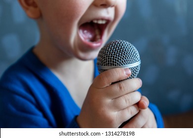 charming kid sings into microphone and opens her mouth wide with milk teeth dropped out.