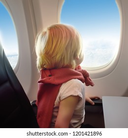 Charming kid traveling by an airplane. Little boy sitting by aircraft window during the flight. Air travel with little kids