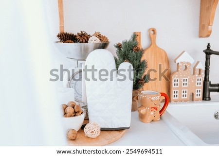 A charming kitchen corner features a white oven mitt, decorative pinecones, and a small tree, creating a warm atmosphere perfect for holiday baking and gatherings during winter.