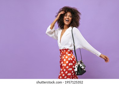 Charming lady with fluffy brunette hair in white shirt smiling on lilac backdrop. Woman in polka dot red trousers posing on isolated background.. - Powered by Shutterstock