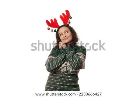Charming Latin American pretty woman in green Xmas patterned sweater and deer antler hoop, sweetly smiling, dreamily looking away at a copy space on white background. Christmas and New Year concept