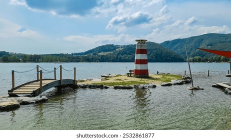 Charming lighthouse on a small island connected by a wooden bridge on lake Stubenbergsee surrounded by rolling hills of East Styrian Hill Country in Styria, Austria. Lush greenery in the background - Powered by Shutterstock