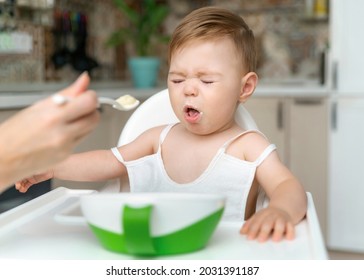 Charming Little Baby Boy 8-11 Months Doesn't Want To Eat Porridge From Spoon With Mom At Home. Kid Doesn't Like Food. No Appetite. Unhappy Child