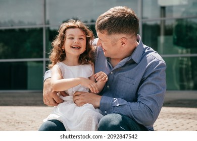 Charming little girl is laughing happily in arms of loving father on summer day on walk in city. Wonderful childhood. Happy relationship. Recreation and adventures. Life insurance. Parental love