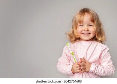charming little girl in pajamas with loose blonde curly hair holds toothbrush in her hands and looks at the camera. concept of oral health, dentistry, happy childhood