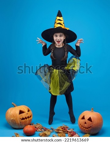 charming little girl in a witch costume jumps in the studio on a blue background.