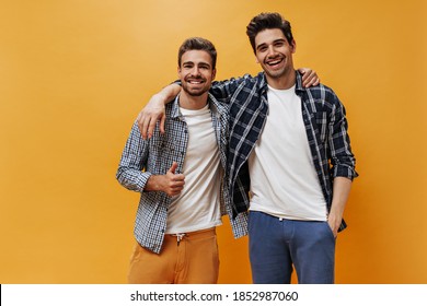 Charming men in checkered shirts and white t-shirt smile on orange background. Cool bearded guy shows peace sign. - Powered by Shutterstock