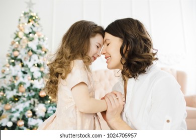 Charming Mom And Her Pretty Little Daughter Pose Before A Rich Christmas Tree In A Luxury White Room