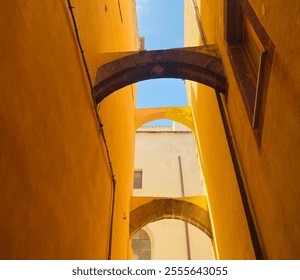 Charming narrow alley with bright yellow walls and historic stone arches under a sunny sky. Great for architecture, travel, and atmospheric imagery. - Powered by Shutterstock