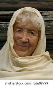 Charming old woman wrapped in a beige scarf. She is smiling and looking very happy.
