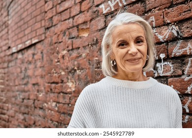 A charming older woman with silver hair leans against a brick wall, enjoying the sunlight. - Powered by Shutterstock