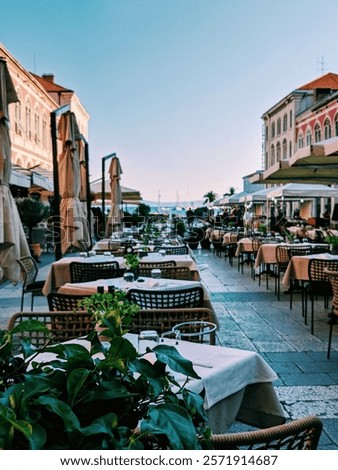 A charming outdoor dining scene in Split Old Town, Croatia, featuring tables lined up along a picturesque street with umbrellas and plants.
