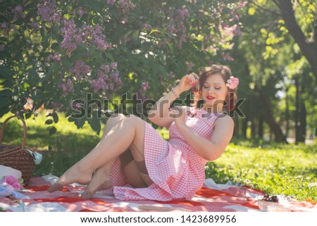 charming pinup girl enjoys a rest and a picnic on the green summer grass. pretty vintage style caucasian woman spend vacantion on city park alone.