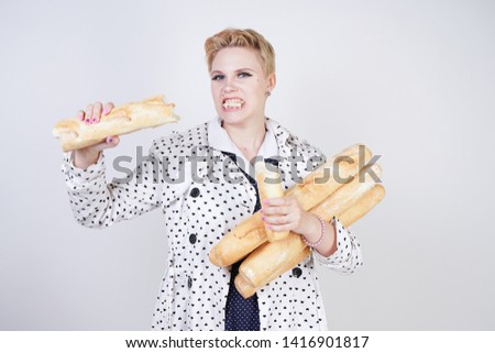 charming pinup woman with short hair in a spring coat with polka dots posing with baguettes and enjoying them on a white background in the Studio. plus size girl in retro clothing holding bread.