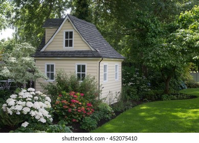 A Charming Playhouse Cottage Sits At The Edge Of A Shaded Perennial Garden.