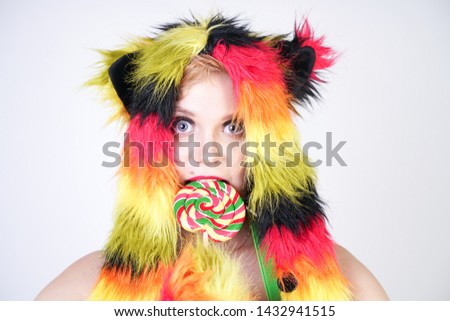 charming plus size young woman in fur hat made of multicolored fibers with cat ears and paws posing in green suspenders, black bra and funny short rainbow skirt on a white background in the Studio