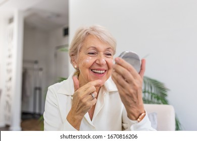 Charming, pretty, old woman touching her perfect soft face skin with fingers, smiling at camera over gray background, using day, night face cream, cosmetology procedures - Shutterstock ID 1670816206