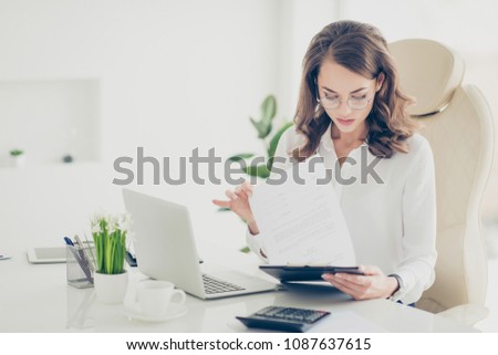 Charming, pretty, stylish, smart, clever financier with curls, hairstyle checking report, examine documents, making control, having clip board with papers in hands sitting on armchair at desk