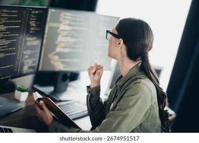 Charming programmer working remotely in a modern workspace while reviewing code on multiple screens and planning project tasks