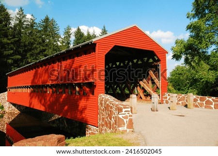 A charming and quaint red covered bridge crosses a stream on a country lane