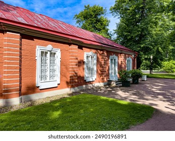 A charming red brick building featuring white framed windows and a red metal roof. Surrounded by lush green trees and a well-kept garden, this scenic structure exudes historical charm and tranquility