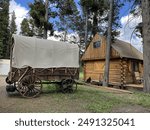 Charming rustic cabin with an old covered wagon in the foreground. The weathered wood and antique wagon evoke a sense of history and nostalgia in this tranquil, picturesque setting.