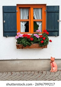 Charming rustic window with geranium flowers and decorative cat statue