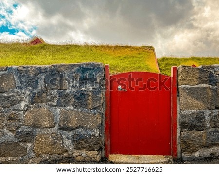 Charming scene of a short red door through a cobblestone wall that leads to red Scandinavian style buildings with natural grass rooftops. Located in Tórshavn, the Capital of the Faroe Islands.