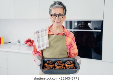 Charming senior woman smiling indoors while holding freshly baked pastries in her home kitchen, showcasing culinary skills - Powered by Shutterstock