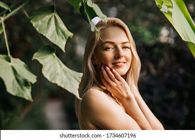 Charming Sensual Caucasian Young Woman Posing In Forest Enjoying Summer Sun And Nature, Touching Face, Using Organic Cosmetics, Applying Sunscreen. Skin Care, Spa Concept.