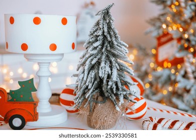 A charming setup features a small, snow-covered Christmas tree beside a polka-dotted lamp. Candy-striped ornaments and twinkling lights create a warm holiday ambiance.