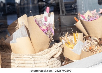 A charming shop window display featuring colorful dried flower bouquets wrapped in kraft paper and nestled in a wicker basket. - Powered by Shutterstock