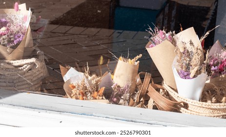 A charming shop window display featuring colorful dried flower bouquets wrapped in kraft paper and nestled in a wicker basket. - Powered by Shutterstock