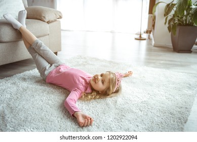 Charming small girl is lying on soft carpet with relaxation in living room. She is looking at camera with happiness and mysterious smile. Domestic comfort concept  - Powered by Shutterstock