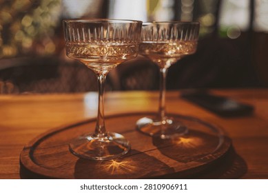 In a charming space filled with soft lighting, two beautiful crystal glasses hold a golden beverage. The wooden surface adds a rustic touch, inviting joyful moments and conversations.