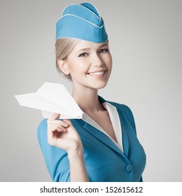 Charming Stewardess Holding Paper Plane In Hand. Gray Background.